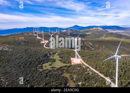 Windpark, Windturbinen und kurvige Straße auf dem Hügel, Luftdrohnenansicht, grüne ökologische Energieerzeugung. Alternative Energieanlage, blaue Wolke Stockfoto