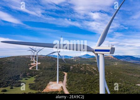 Windpark, Windturbinen und kurvige Straße auf dem Hügel, Luftdrohne Ansicht. Grüne ökologische Energieerzeugung. Alternative Energieanlage, blaue Wolke Stockfoto