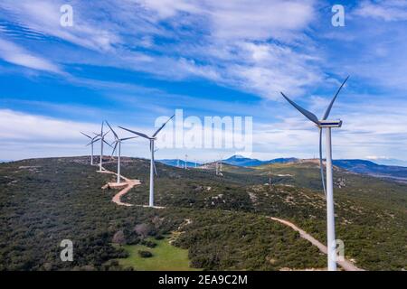 Windpark, Windturbinen und kurvige Straße auf dem Hügel, Grüne ökologische Energieerzeugung. Alternative Energieanlage, blauer wolkiger Himmel, sonniger Tag, G Stockfoto