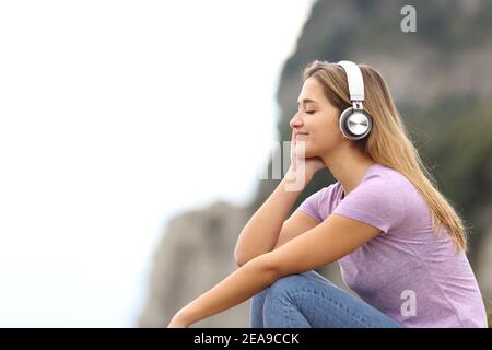 Profil einer entspannten Frau, die kabellos Musik hört Kopfhörer in den Bergen Stockfoto