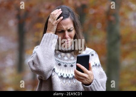 Traurige Frau beschwerte sich beim Überprüfen des Smartphones im Winter in einem parken Stockfoto