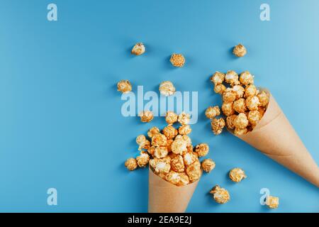 Karamell Popcorn in einem Papierumschlag auf blauem Hintergrund. Köstliches Lob für das Ansehen von Filmen, Serien, Cartoon. Freier Speicherplatz, Nahaufnahme. Minimalis Stockfoto