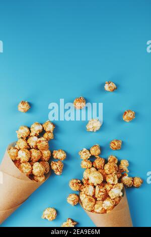 Karamell Popcorn in einem Papierumschlag auf blauem Hintergrund. Köstliches Lob für das Ansehen von Filmen, Serien, Cartoon. Freier Speicherplatz, Nahaufnahme. Minimalis Stockfoto