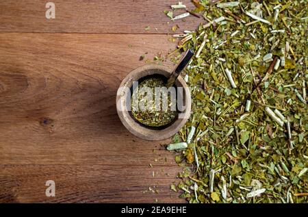 Traditionelle Mate aus Kalabash über einem Holztisch mit Yerba Mate darüber verstreut. Stockfoto