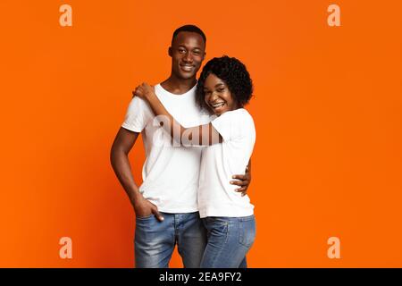 Fröhliche schwarze Paar in der Liebe Umarmung auf orange Stockfoto