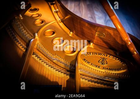 Das Resonanzboden eines Steinway M, der durch ein Fenster über dem Klavier von etwas Sonnenlicht beleuchtet wird. Es ruht auf einem dicken Hartholzboden. Stockfoto