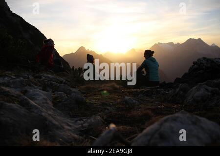 3 junge Frauen im Sonnenuntergang in Richtung Wettersteingebirge, aufgenommen auf dem Gamseck oberhalb der Mittenwalder Hütte Stockfoto