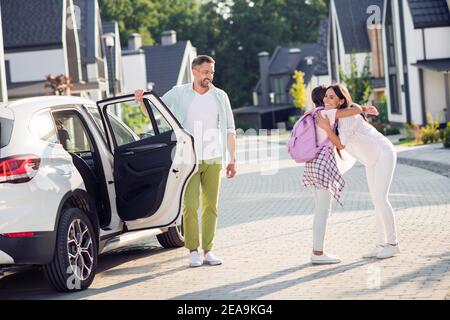 Foto-Porträt des Mädchens umarmt Mutter kommt zurück von der Schule Verlassen des weißen Autos im Freien Stockfoto