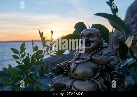 Buddha Figur, bei Sonnenuntergang, auf einer Klippe im Meer Stockfoto