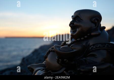 Buddha Figur, bei Sonnenuntergang, auf einer Klippe im Meer Stockfoto