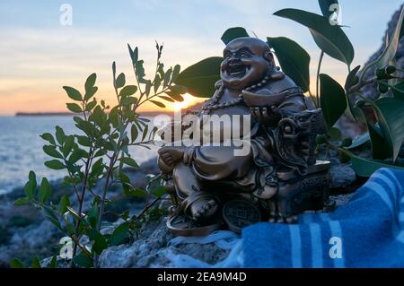 Buddha Figur, bei Sonnenuntergang, auf einer Klippe im Meer Stockfoto