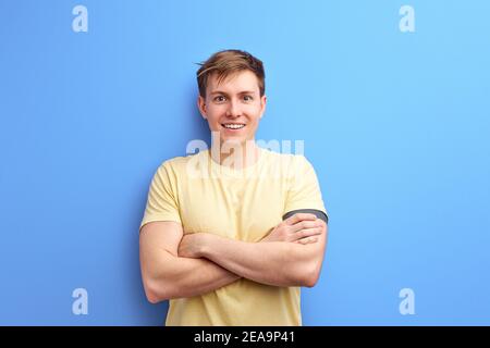 Inspiriert männlich in casual T-Shirt tragen steht lächelnd mit Armen gefaltet. Isoliert über blauen Studio-Hintergrund. Lifestyle, Menschen, menschliche Emotionen Konzept Stockfoto
