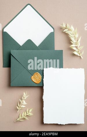 Hochzeit Details Einladung Vorlage. Minimalistische Hochzeitskarte und grüne Umschläge auf pastellbeigem Hintergrund mit getrockneten Blumen. Flach liegend, Draufsicht. Stockfoto