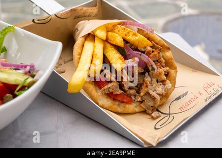 Folegandros, Griechenland - 24. September 2020: Traditionelles griechisches Souvlaki mit Chicken Gyros, Gemüse und Pommes in Pita-Brot serviert. Stockfoto