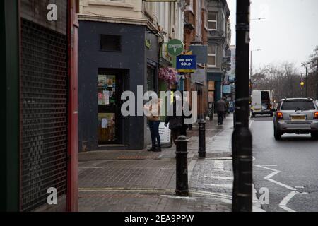 Schnee in London - EINE Frau, die eine Maske trägt, desinfiziert ihre Hände vor einem Geschäft - Fußgänger, die in Hüte und Schals eingewickelt sind, pendeln im Schnee nach Hause, londoner Busse, Straßenszenen 08/02/2021 Credit: London Evening Standard/Alamy Live News Stockfoto