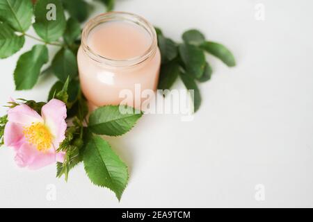 Aromatische kosmetische Produkte auf weißem Tisch Kopieplatz. Glasflasche mit Extrakt, Tonic mit Blütenblättern, frische rosa Rose, natürliche Bio-ma infundiert Stockfoto