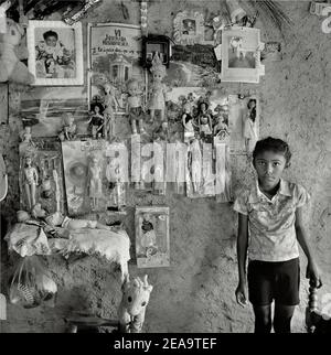 Junges Mädchen vor Puppen, die an der Wand einer einfachen Hütte in einem armen Viertel, Venezuela, Südamerika, hängen. Stockfoto