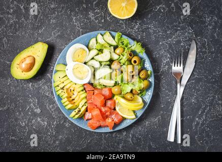 Ketogene, paleo Diät-Schüssel mit gesalzenem Lachs Fisch, Zitrone, Avocado, Oliven, gekochtem Ei, Gurke, grünem Salat, gesunde Ernährung Trend Stockfoto