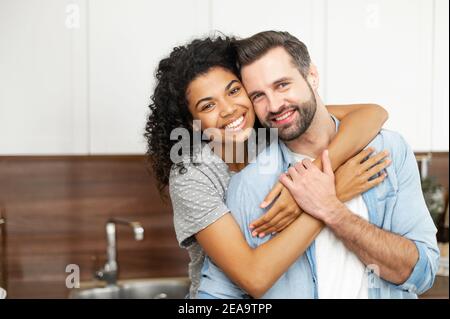 Nahaufnahme von glücklichen interracial Paar posiert über verschwommene Küche Hintergrund, glückliche Besitzer der neuen Wohnung lächeln und Blick auf die Kamera, junge Afrikaner Stockfoto