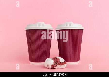Pappkaffeetassen und ein Cookie, symmetrisch auf rosa Hintergrund angeordnet Stockfoto