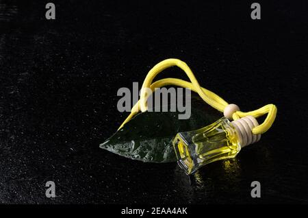 Eine Flasche gelber Flüssigkeit mit einem Holzstopfen und einem grünen Blatt Zitronenbaum mit Wassertröpfchen auf einem schwarzen Holzhintergrund. Aromatische Öle. Selektiv Stockfoto
