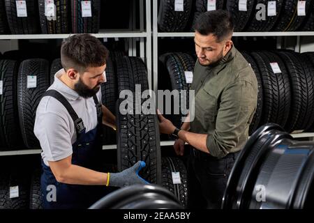 Mechaniker und Kunde sprechen über Reifen in der Reparaturwerkstatt, Austausch von Winter- und Sommerreifen. Saisonales Reifenaustauschkonzept. Kunde ist ch Stockfoto