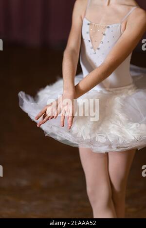 Junge Ballerina mit gekreuzten Händen und Beinen in weißem Ballettrock auf der Bühne. Ballett-Performance-Konzept Stockfoto