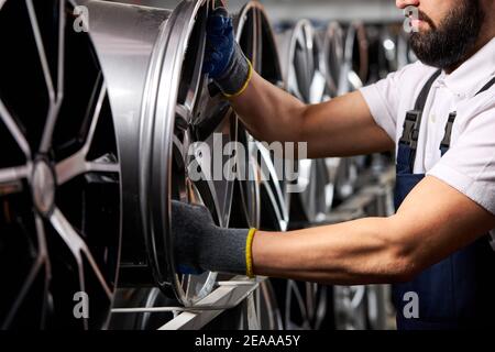 Nahaufnahme des Mannes in Handschuhen, die Auto-Felgen aus dem Regal nehmen, beschnitten Auto Mechaniker in Uniform bei der Arbeit Stockfoto