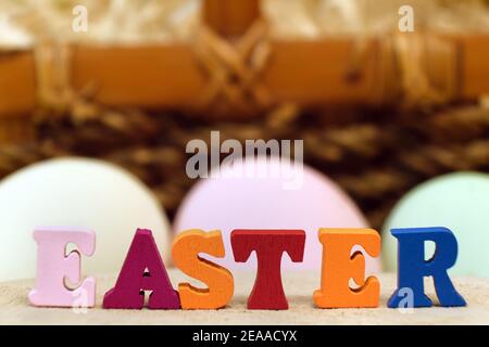 Wort Ostern von bunten Spielzeug Alphabet Buchstaben auf Holztisch, bemalte Eier und Korbkorb Hintergrund. Ideal für die Gestaltung von hellen Grußkarten Stockfoto