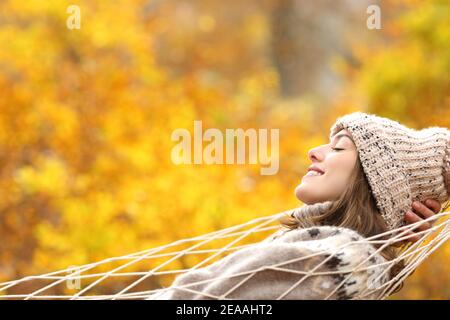 Seitenansicht Porträt einer glücklichen Frau, die sich entspannt im Liegen Eine Hängematte im Herbst im Wald Stockfoto