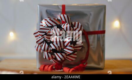 Weihnachtsgeschenk in Silber mit großer roter Schleife mit Adventsstern, Weihnachtsstern oder Weihnachtsstern in Rot vor einer Lichterkette, romantische, weihnachtliche Atmosphäre Stockfoto
