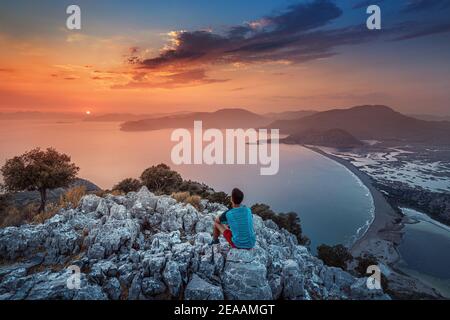 Allein der Mann sitzt auf einem Felsen und bewundert den bunten Sonnenuntergang. Das Konzept der individuellen Psychologie und des Solo-Reisens auf der Suche nach sich selbst. Stockfoto