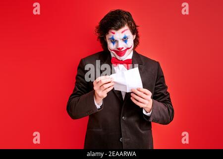 Männliche Magier Durchführung eines Tricks mit Händen isoliert auf rotem Hintergrund, mit bunten halloween Make-up auf Gesicht Stockfoto