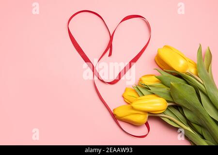 Blumenstrauß aus gelben Tulpen und Herz aus roten Bändern auf rosa Hintergrund mit Kopierfläche. Geschenkkonzept zum Muttertag oder Valentinstag Stockfoto