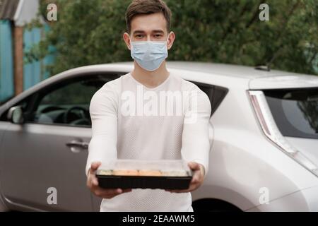 Sushi-Set in Box gesunde Lebensmittel Lieferung Online-Service mit dem Auto. Schöner Mann Kurier in medizinische Maske gibt Sushi-Box zu Ihnen. Japanische Küche: Brötchen, so Stockfoto