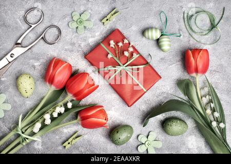 Ansicht von oben, flach liegend. Arrangement von Ostern, Frühlingsdekorationen. Eingewickelte Geschenke, rote Tulpe und Maiglöckchen Blumen und Ostereier Stockfoto