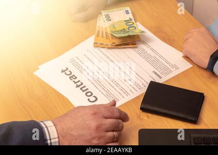 Selektiver Fokus auf einen Vertrag und Geld auf die gesetzt Tabelle bereit, ein Geschäft oder Erpressung auf einem zu machen Holztisch mit Laptop und Handy-Konzept Stockfoto