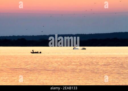 Grand Lake O' The Cherokees in Grove Oklahoma ist bei Fischern sehr beliebt, wie auf diesem Foto von drei Booten auf dem Wasser bei Sonnenuntergang zu sehen ist. Stockfoto