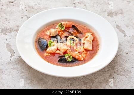 Portion Tomatensuppe mit Meeresfrüchten auf weißem Teller Restauranttisch Stockfoto
