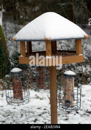 Eine Vogelfütterungsstation mit Vogelfutterhäuschen für im Winter schneebedeckte Wildgartenvögel. Stockfoto