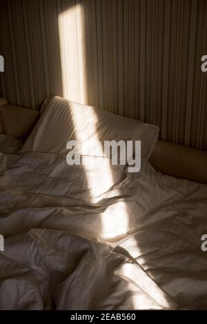 Sonnenstrahl fällt auf das Bett. Die Sonne strahlt am Morgen durch das Fenster. Neuer Tag mit warmem Sonnenlicht Flare. Stockfoto