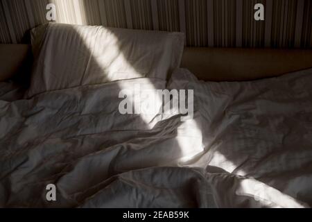 Sonnenstrahl fällt auf das Bett. Die Sonne strahlt am Morgen durch das Fenster. Neuer Tag mit warmem Sonnenlicht Flare. Stockfoto