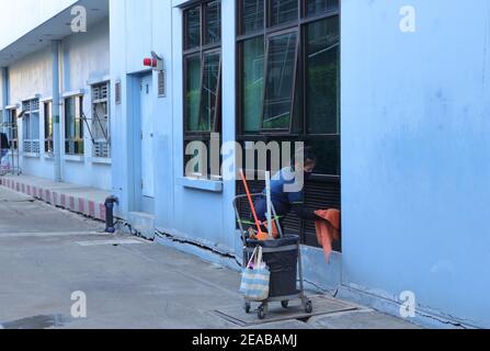 Bangkok, Thailand - 2. Februar 2021 : Arbeiterin trägt Gesichtsmaske wischen Lüftungsgitter von Tuch außerhalb des Gebäudes, das Tuch ist in Bewegung Stockfoto