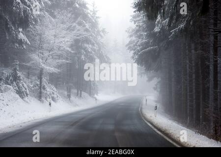 Winterberg, Sauerland, Nordrhein-Westfalen, Deutschland - verschneite Landschaft im Wald mit einer leeren Landstraße. Stockfoto