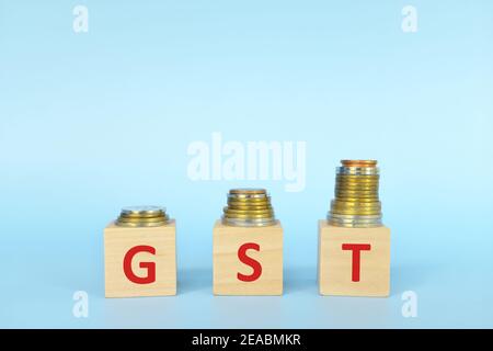 GST-Buchstaben auf Holzblöcken in blauem Hintergrund erhöhen Stapel von Münzen. Erhöhung des Steuerkonzepts für Waren und Dienstleistungen. Stockfoto