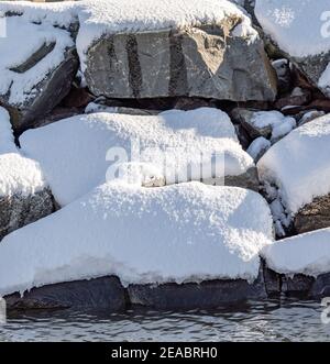 Große Felsbrocken, die vom Wasser mit Schnee bedeckt sind Stockfoto