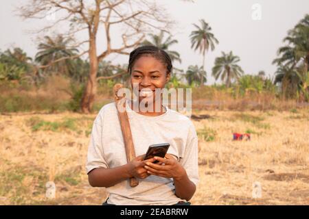 Eine afrikanerin, die mit ihrem Smartphone von der Farm plaudert Stockfoto