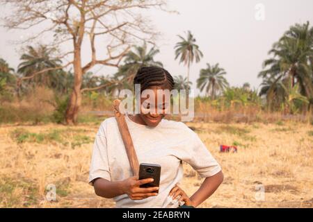 Eine afrikanerin, die mit ihrem Smartphone von der Farm plaudert Stockfoto