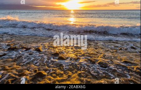 Golden Sunset - heller Sonnenuntergang Blick auf starke Wellen rauschen in und aus der felsigen Küste an der Nordwestküste von Maui Island, Hawaii, USA. Stockfoto