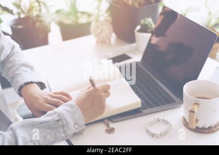 Frau schreibt in Planner Notebook, während mit Laptop arbeiten oder planen mit Arbeitsplatz zu Hause. Bildung Business Lifestyle Konzept. Stockfoto
